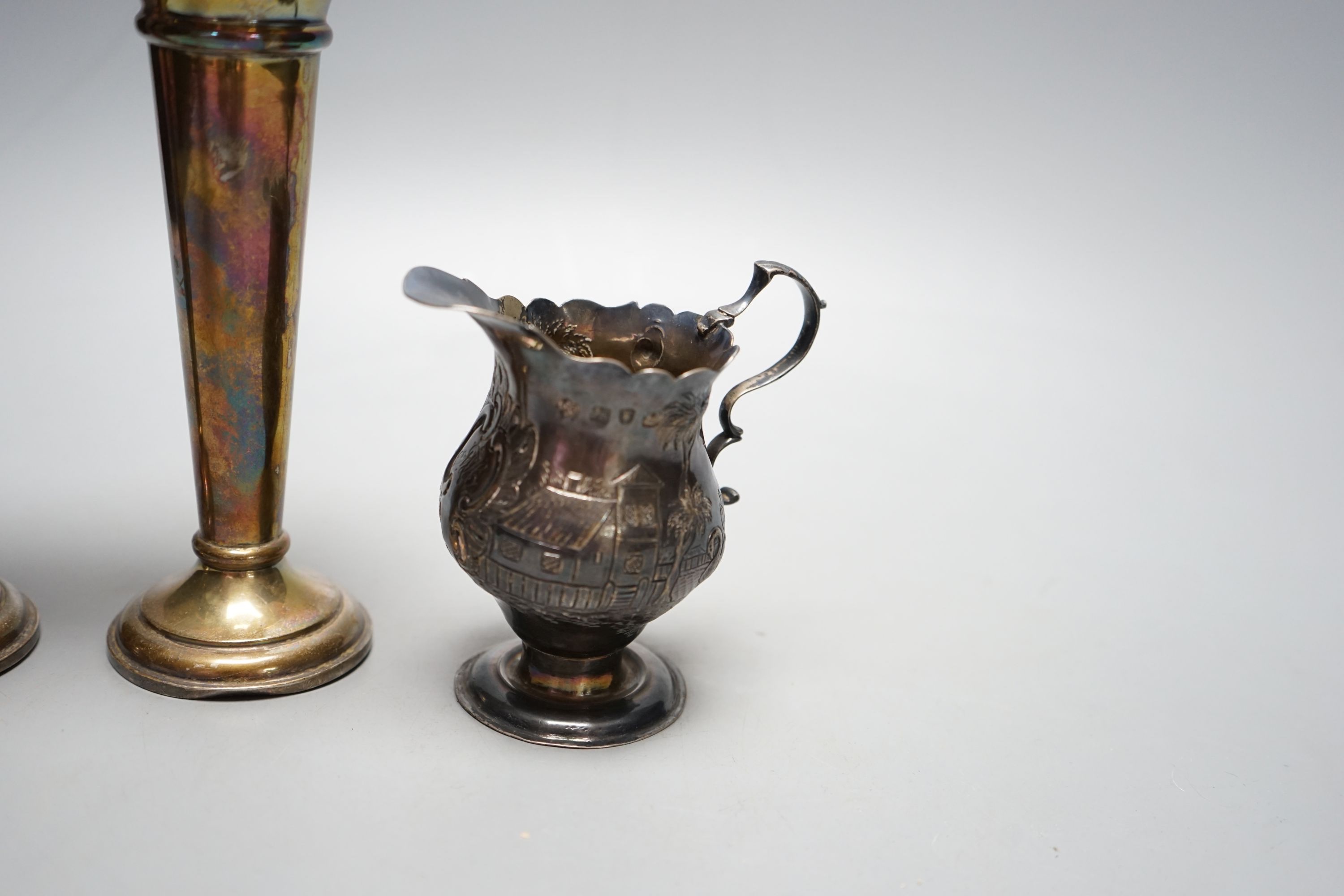A George III silver helmet shaped cream jug, with later embossed decoration, London, 1759, 97mm and a pair of Edwardian silver spill vases, 16.3cm.
